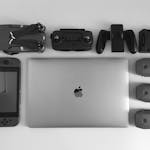 A black and white flat lay of various modern tech gadgets including a laptop, drone, and gaming device.