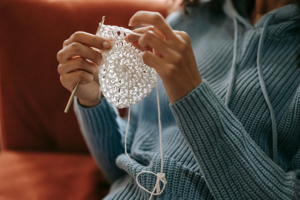 Woman wearing a crochet outfit and handing weaving a crochet item.