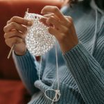 Woman wearing a crochet outfit and handing weaving a crochet item.